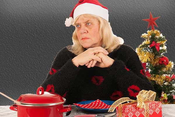 Deprimeret kvinde med nissehue foran juletræ.